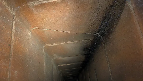 A cracked clay flue tile with soot staining running along the fracture